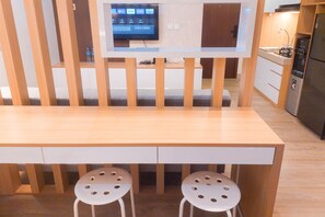 A modern kitchen with a wooden table and two stools, a TV mounted on the wall, and a refrigerator. - Cozy Studio Apartment Parkland Avenue (South Tangerang)