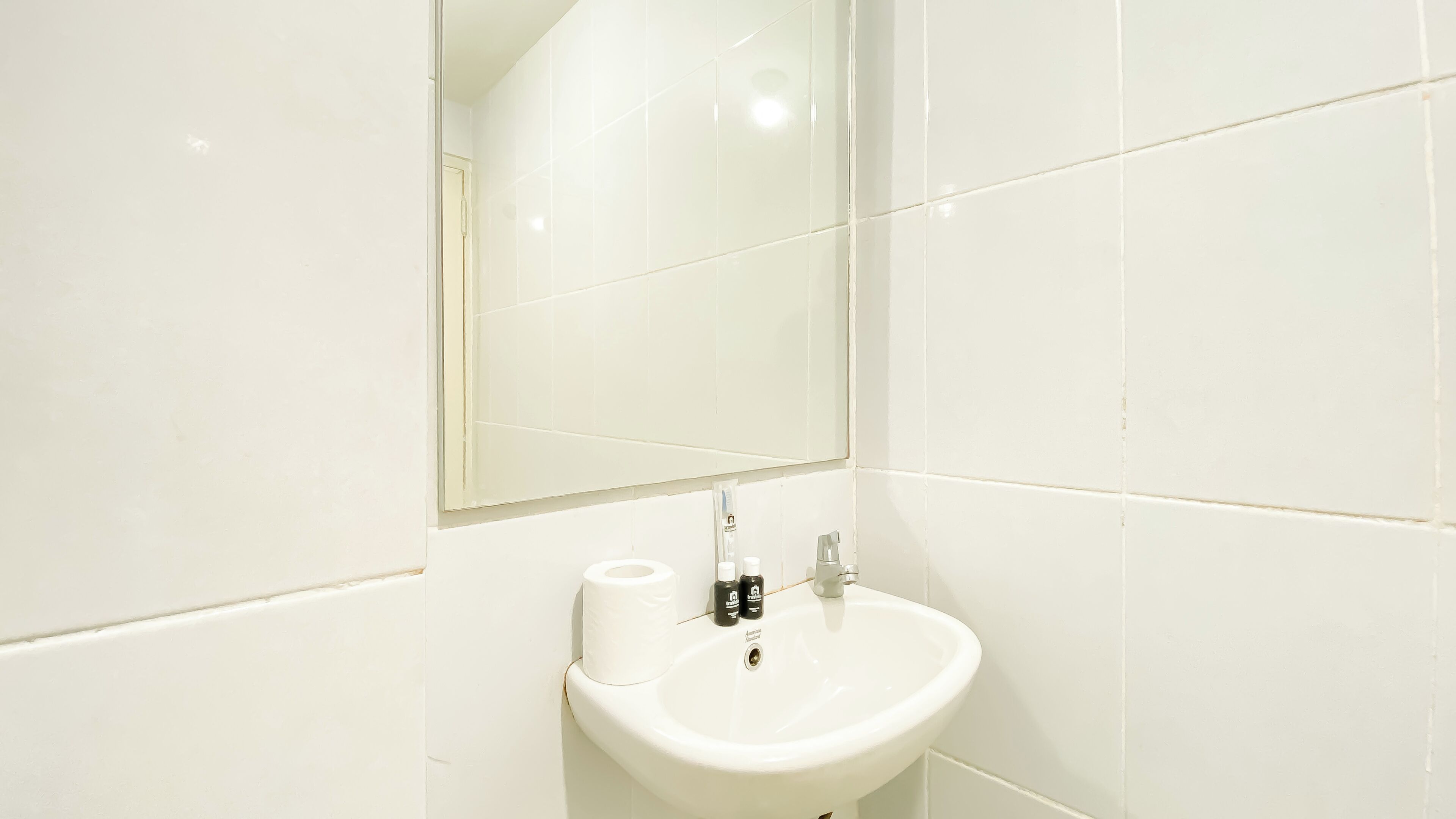 A white bathroom with a sink, mirror, and toilet paper.