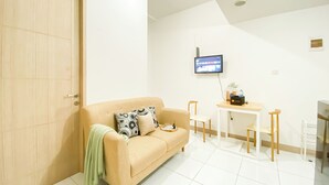 A modern living room with a beige sofa, a small table, and a TV mounted on the wall. - Comfy And Lovely 2Br Apartment Tokyo Riverside Pik 2 (Teluknaga)