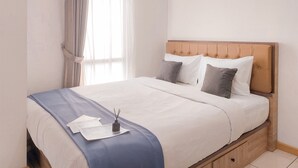 A neatly made bed with a blue bedspread, white pillows, and a wooden headboard. - Comfy 1Br Apartment At M-Town Residence (Gading Serpong)