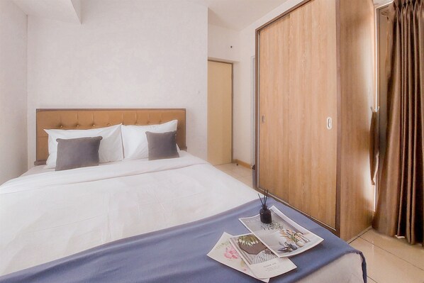 Une chambre d’hôtel avec un grand lit, une armoire en bois et une table de chevet sur laquelle se trouvent un magazine et une bouteille.