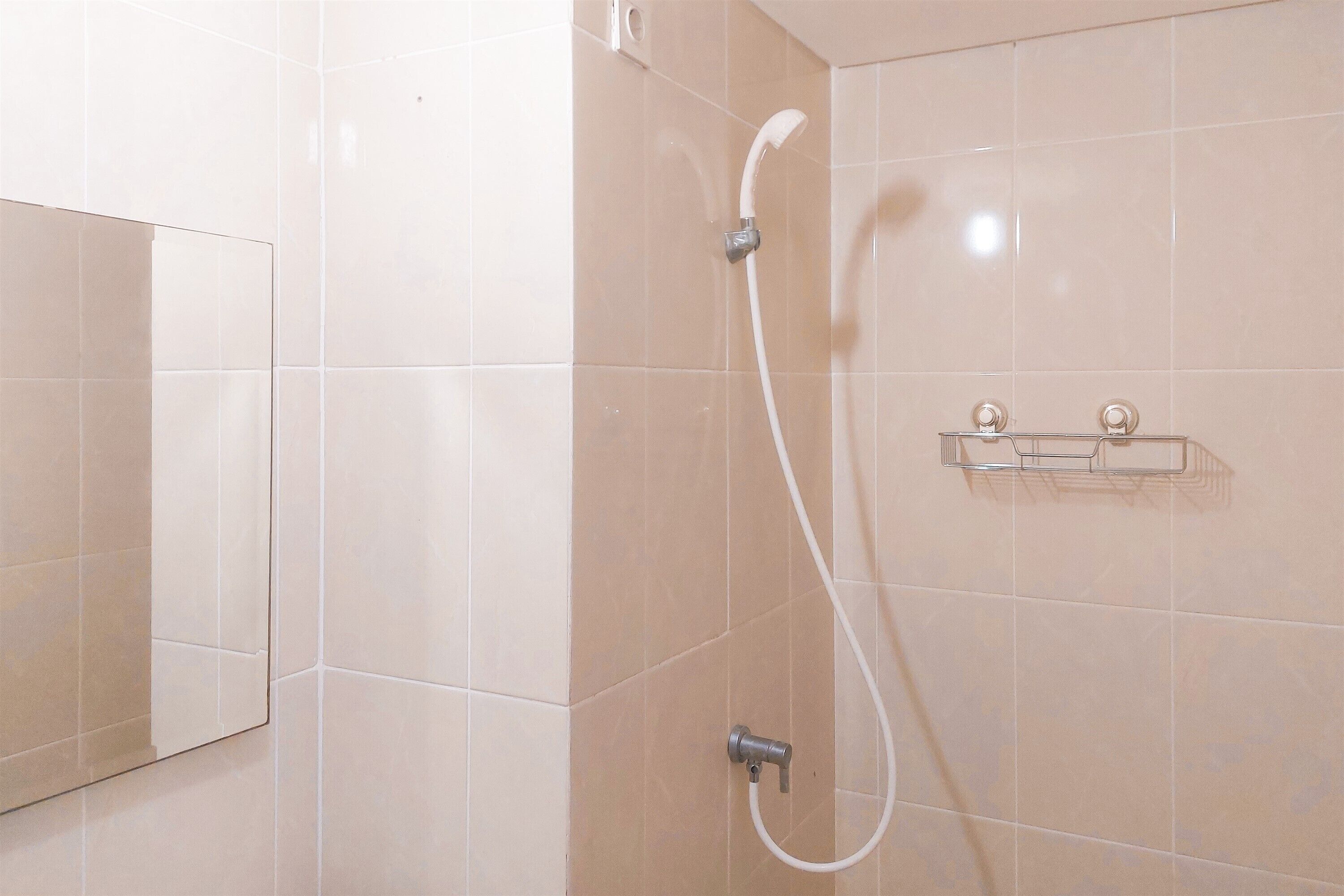A bathroom with beige tiles, a shower with a handheld showerhead, and a clear shelf unit.