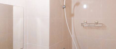 A bathroom with beige tiles, a shower with a handheld showerhead, and a clear shelf unit.