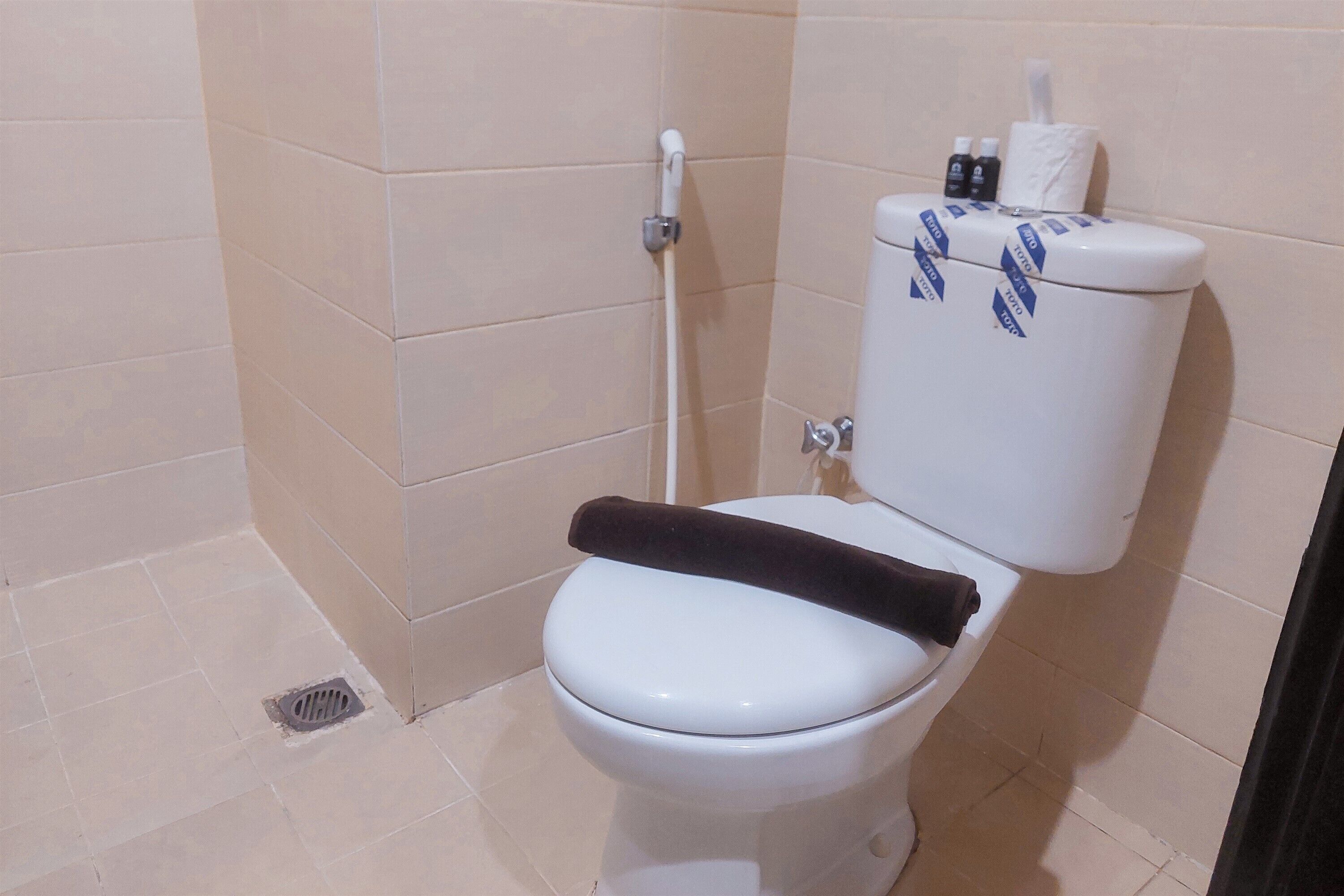 Eine weiße Toilette mit einem schwarzen Toilettenpapierhalter und einer Toilettenpapierrolle.