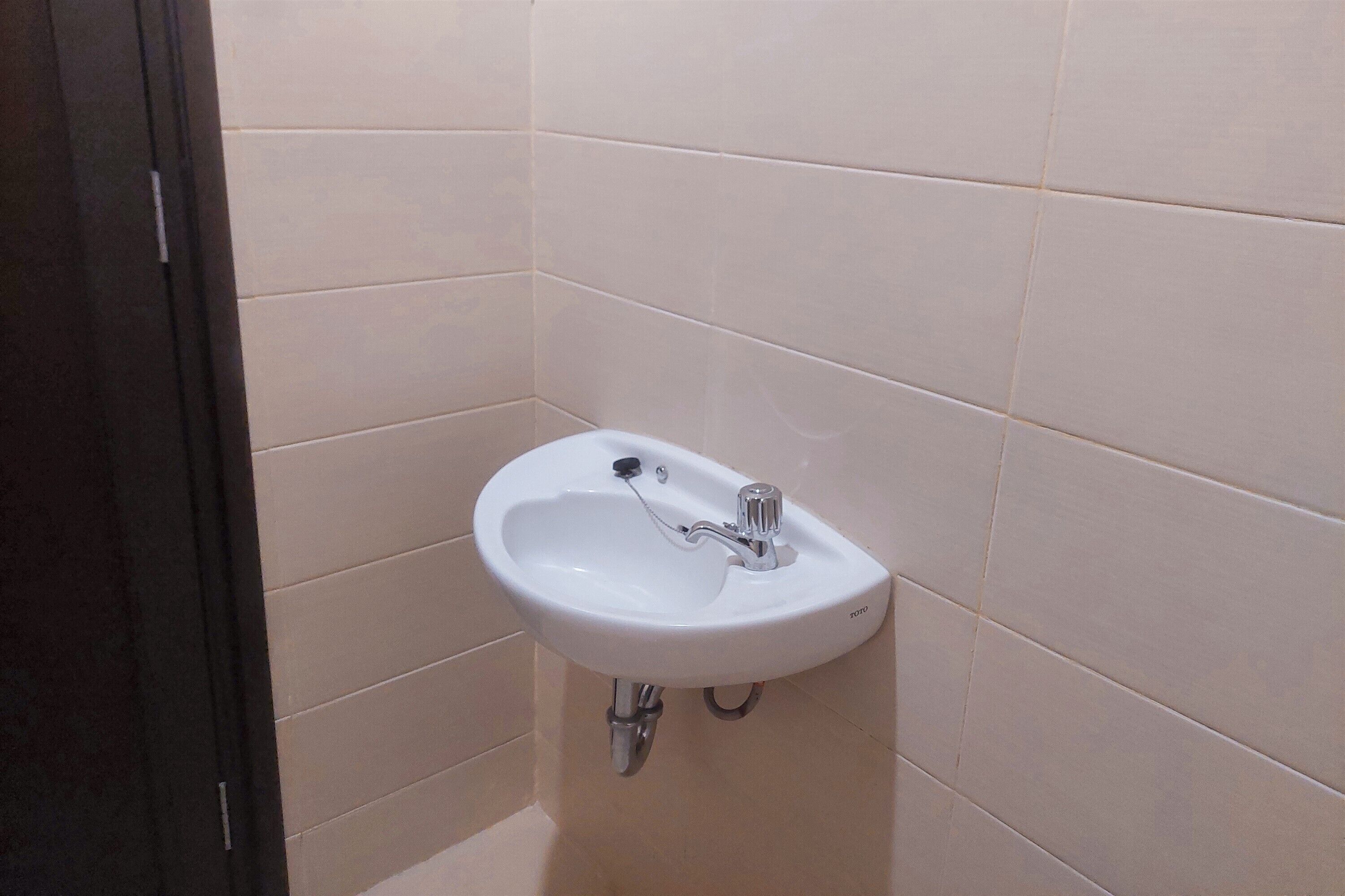 A white bathroom sink with a chrome faucet, mounted on a beige tiled wall.