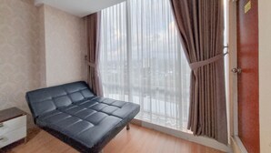 A room with a bed, a window with curtains, a door, and a small table. - Relaxing And Stylish Studio At Mataram City Apartment (Ngaglik)