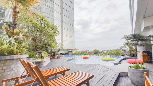 A rooftop pool area with lounge chairs, potted plants, and a modern building in the background. - Relaxing And Stylish Studio At Mataram City Apartment (Ngaglik)