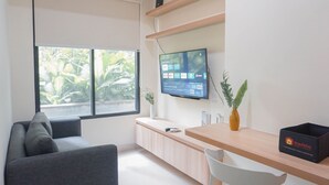 Una habitación moderna con sofá, escritorio de madera, televisión y ventana con vista a zonas verdes.