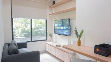 A modern room with a sofa, a wooden desk, a TV, and a window with a view of greenery.
