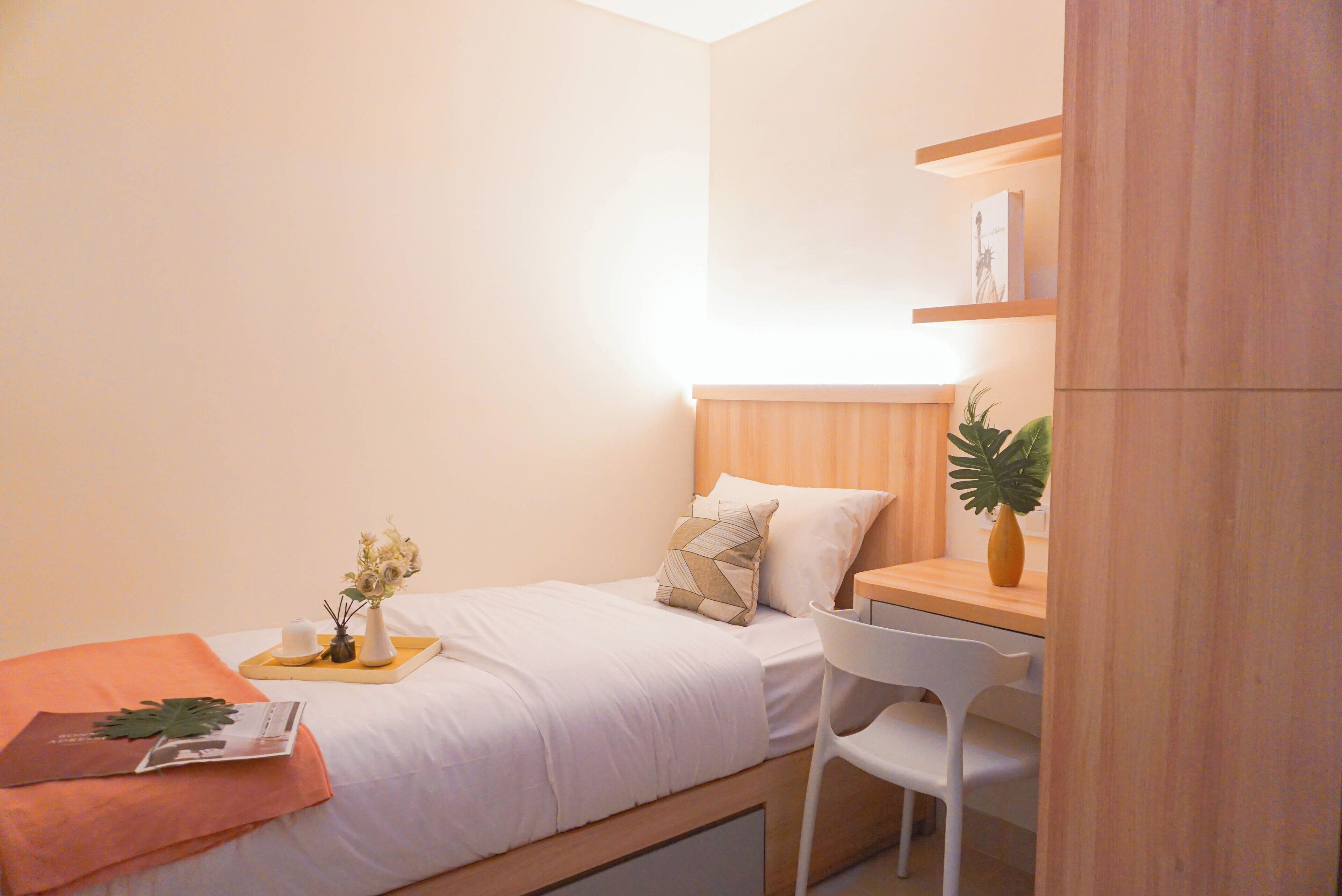 Ein kleines, aufgeräumtes Schlafzimmer mit Bett, Nachttisch, Stuhl und einer kleinen Schreibtischzeile.