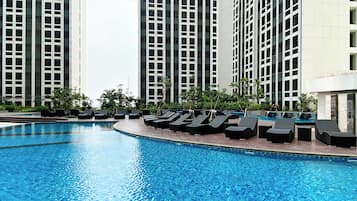 A swimming pool with lounge chairs and tall buildings in the background.