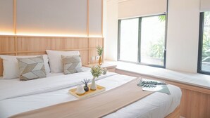 Una habitación de hotel moderna con una cama grande, una mesita de noche con un jarrón de flores y una ventana con vistas a zonas verdes.