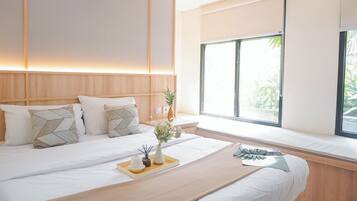 A modern hotel room with a large bed, a bedside table with a vase of flowers, and a window with a view of greenery.