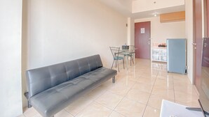 A living room with a black sofa, a dining table with chairs, a blue refrigerator, and a tiled floor. - Scenic View 2Br At Apartment Tamansari Panoramic (Bandung)