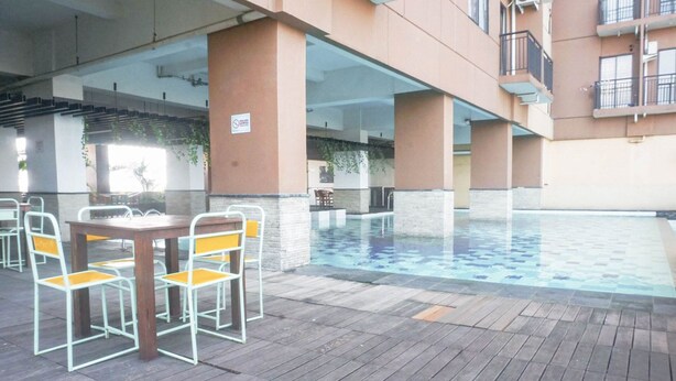 An outdoor pool area with a table and chairs, surrounded by a building with balconies. - Scenic View 2Br At Apartment Tamansari Panoramic (Bandung)