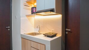 Una cocina compacta con un lavamanos, una balanza y una tetera sobre la encimera.
