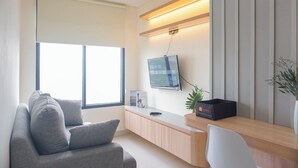 Una sala de estar moderna con un sofá gris, una silla blanca, una consola de madera con televisor de pantalla plana, una planta en maceta y una ventana con persianas.