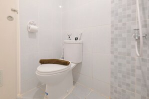 A bathroom with a toilet, a towel on the seat, a toilet paper holder, and a shower area with a tiled wall. - Great Choice And Homey 2Br Apartment Tokyo Riverside Pik 2 (Teluknaga)