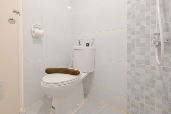 A bathroom with a toilet, a towel on the seat, a toilet paper holder, and a shower area with a tiled wall.