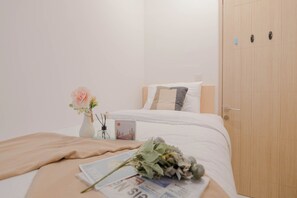 A neatly made bed with a beige blanket, a white pillow, and a small vase with a pink flower. - Great Choice And Homey 2Br Apartment Tokyo Riverside Pik 2 (Teluknaga)