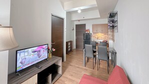 En moderne stue med fjernsyn, en rød sofa og et spiseområde med stole og et bord.