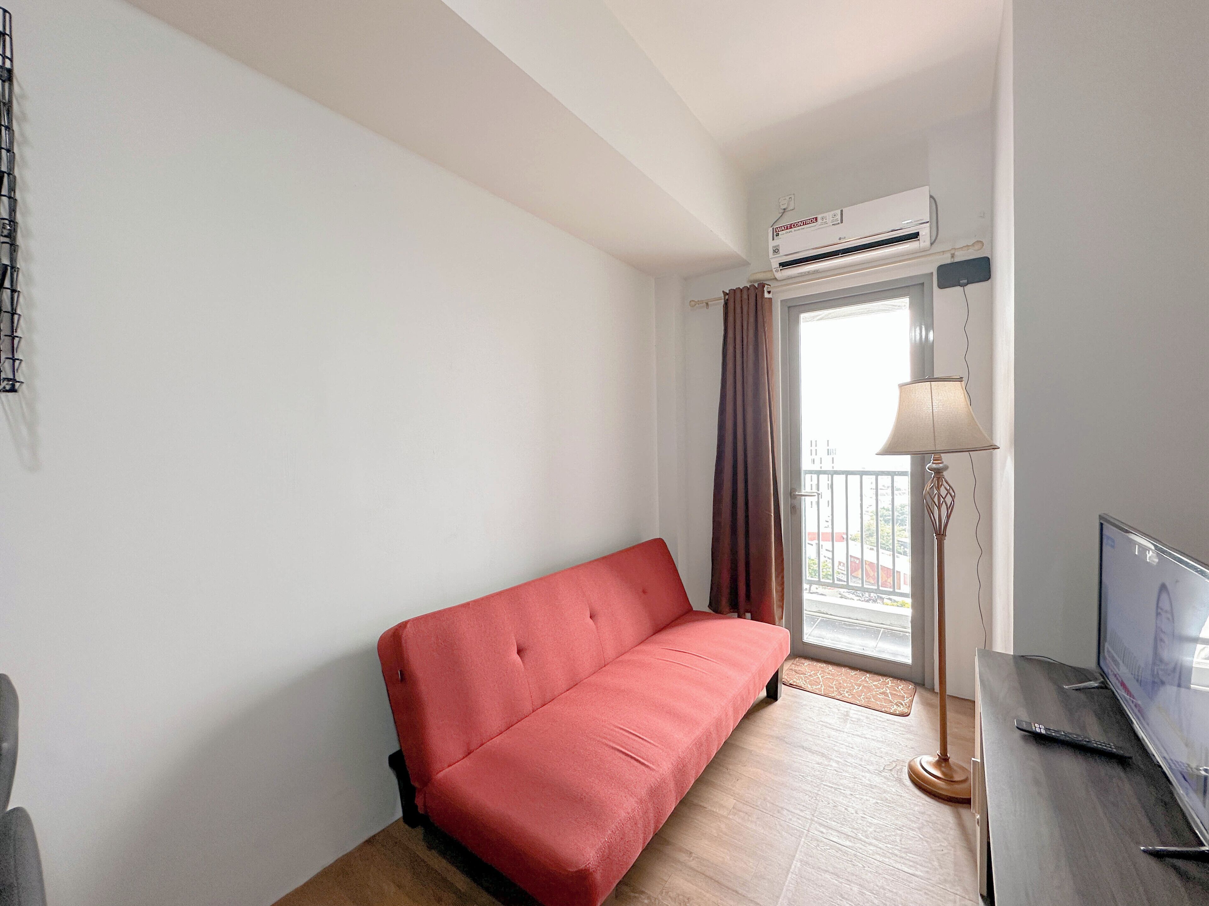 Ein Zimmer mit einem roten Sofa, einem Fernseher und einer Klimaanlage.