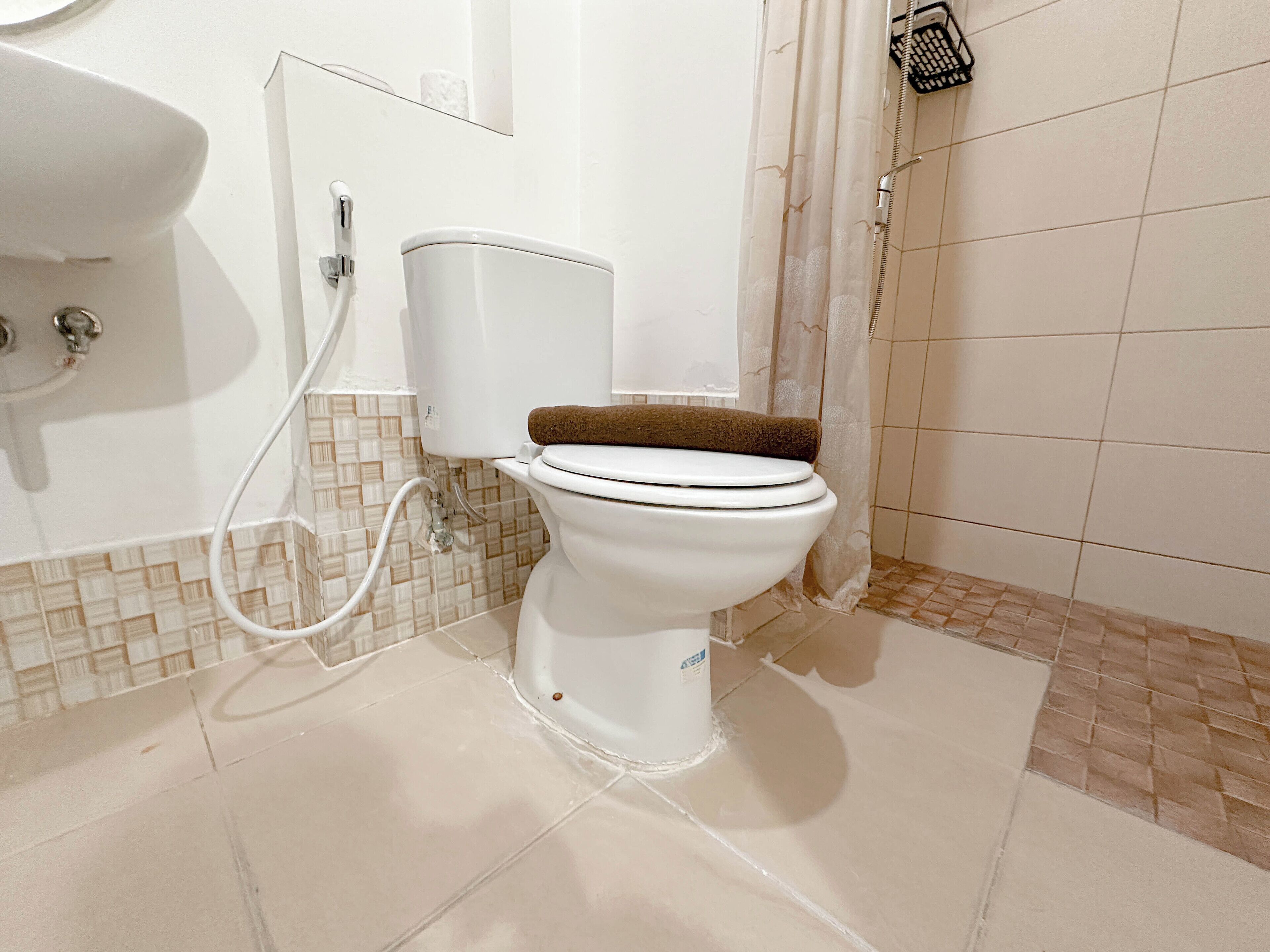 A white toilet with a brown seat and a white tank, connected to a wall-mounted sink and a shower with a glass door.