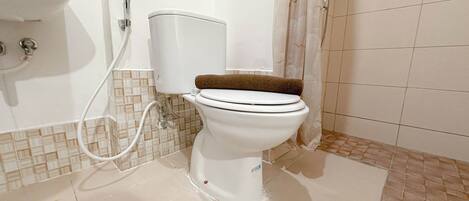 A white toilet with a brown seat and a white tank, connected to a wall-mounted sink and a shower with a glass door.
