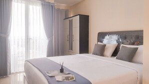 Ένα στρωμένο κρεβάτι με κεφαλάρι, μια ντουλάπα και ένα παράθυρο με κουρτίνες.