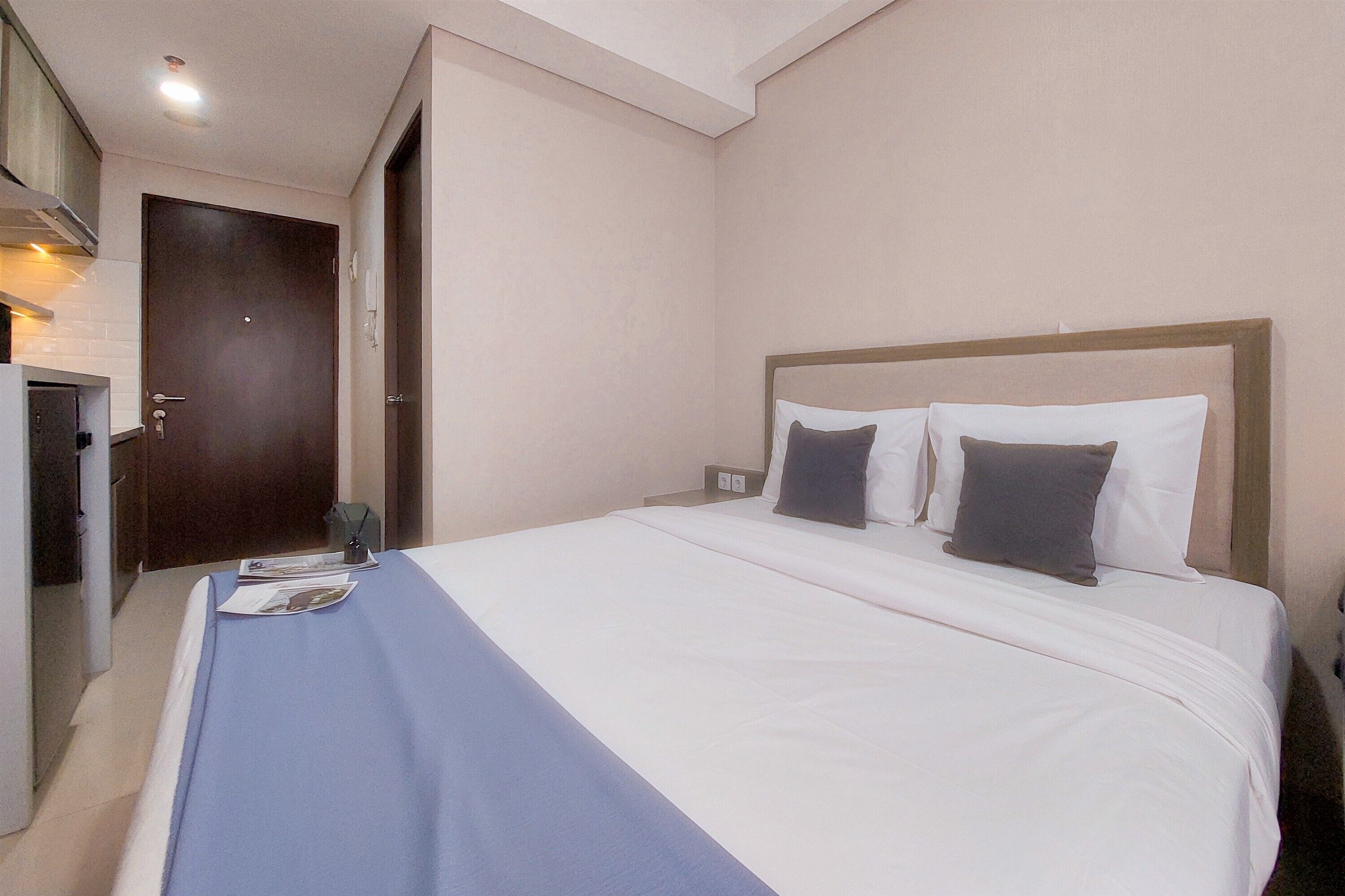 A hotel room with a bed, a nightstand, a door, and a small table with a lamp.