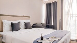 Ein ordentlich bezogenes Bett mit blauer Bettdecke, weißen Kissen und einer kleinen Vase mit Räucherstäbchen.