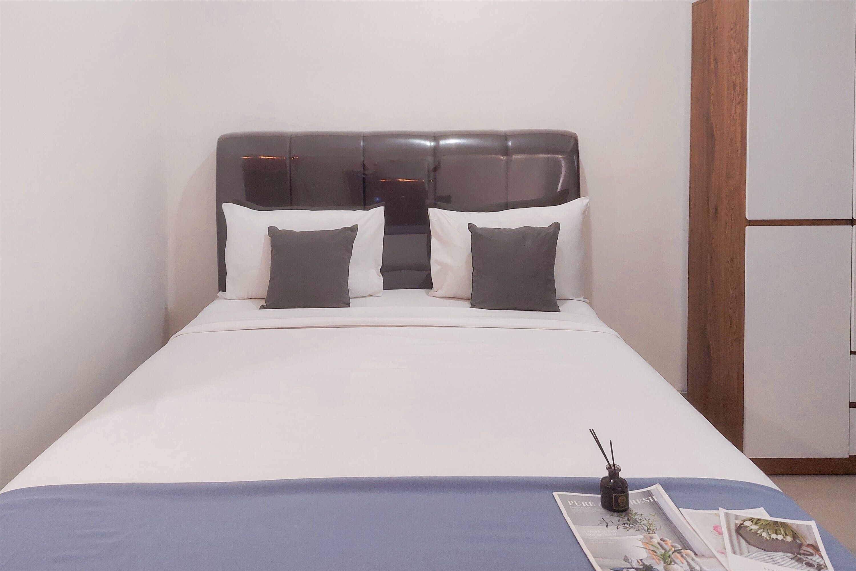 A neatly made bed with a grey headboard, white bedding, and a blue accent at the foot.