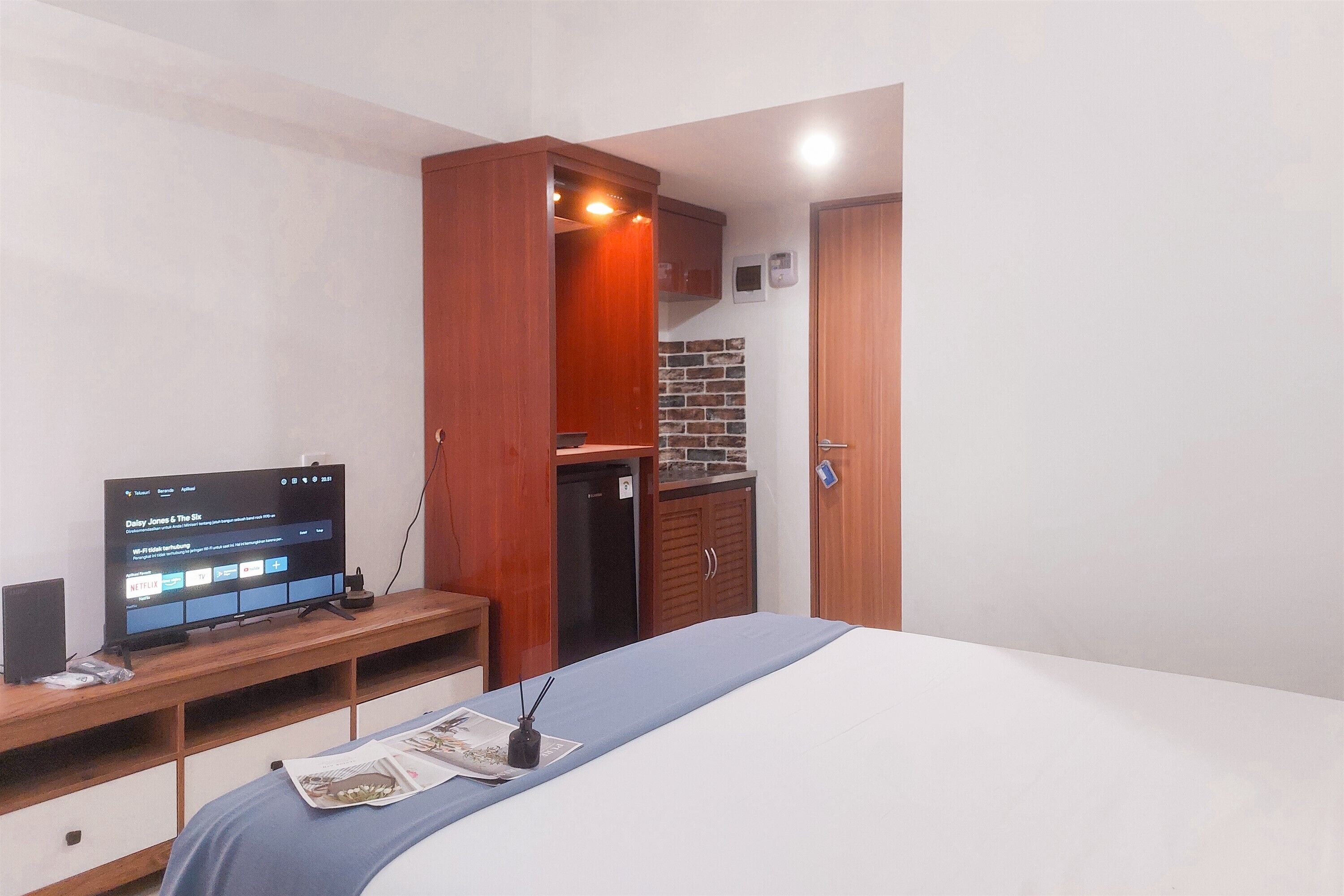 Une chambre à coucher avec un lit, un téléviseur posé sur un meuble en bois, un petit réfrigérateur et une armoire en bois.