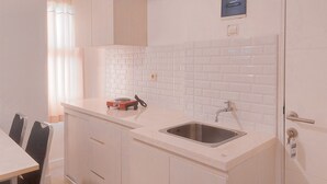 A modern kitchen with white cabinets, a stainless steel sink, and a small countertop with a kettle.