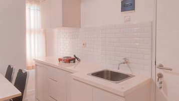A modern kitchen with white cabinets, a stainless steel sink, and a small countertop with a kettle.