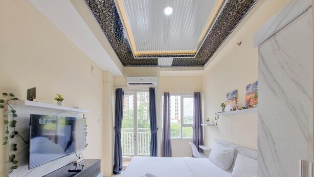 Ein modernes Hotelzimmer mit einem großen Bett, einem Flachbildfernseher, einer Decke mit einem Dekor und einem Balkon mit Vorhängen.