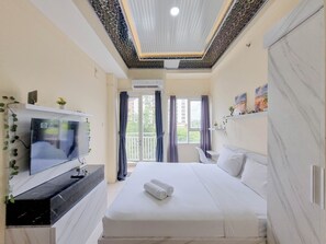 A modern hotel room with a large bed, a flat-screen TV, a ceiling with a decorative pattern, and a balcony with curtains. - Best Deal Studio Malioboro City Apartment (Yogyakarta)