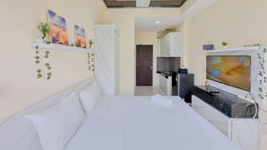 Ein Hotelzimmer mit einem Bett, einem Fernseher, einer kleinen Küchenzeile und einer Tür zu einem weiteren Raum.
