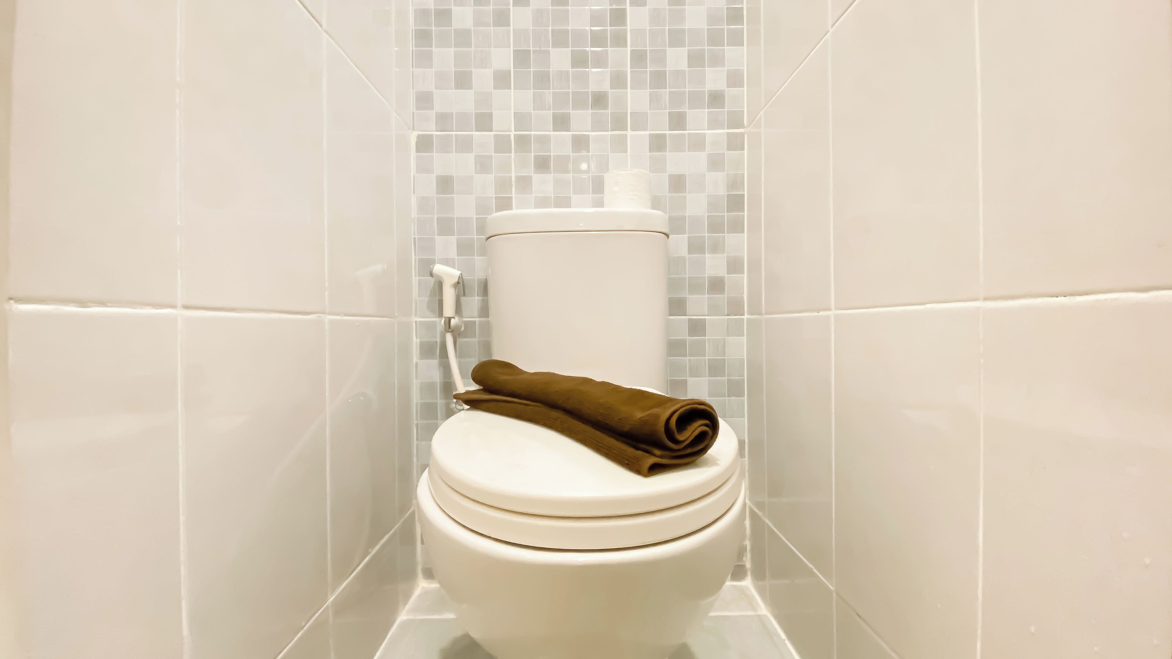 Inodoro con asiento y tapa blancos, una toalla marrón encima y un botón de descarga blanco.