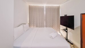 Habitación de hotel con cama, televisor montado en la pared y ventana con cortinas.