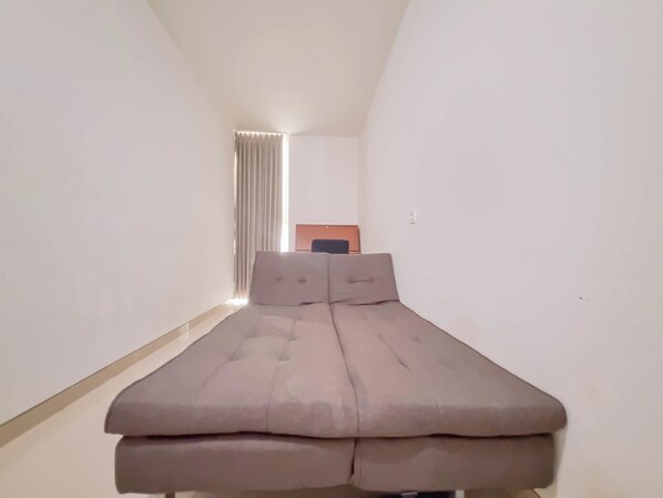 A narrow room with a bed, a desk, and a chair.