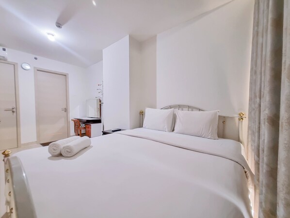 A hotel room with a large bed, a desk with a chair, a mirror, and a wardrobe. - Cozy And Enjoy Living 1Br At Mataram City Apartment (Ngaglik)