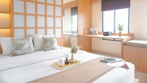 A modern hotel room with a large bed, a wooden partition wall, a desk with a window, and a small plant.