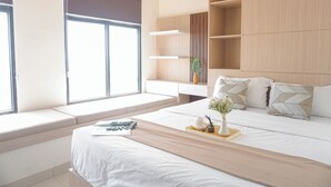 A modern bedroom with a large bed, built-in shelves, a window seat, and a bedside table with a vase and book. - Comfy Abode 2Br Apartment Pollux Chadstone (Cikarang)
