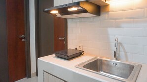 A compact kitchen with a built-in stove, a stainless steel sink, and a wooden door. - Comfy Abode 2Br Apartment Pollux Chadstone (Cikarang)