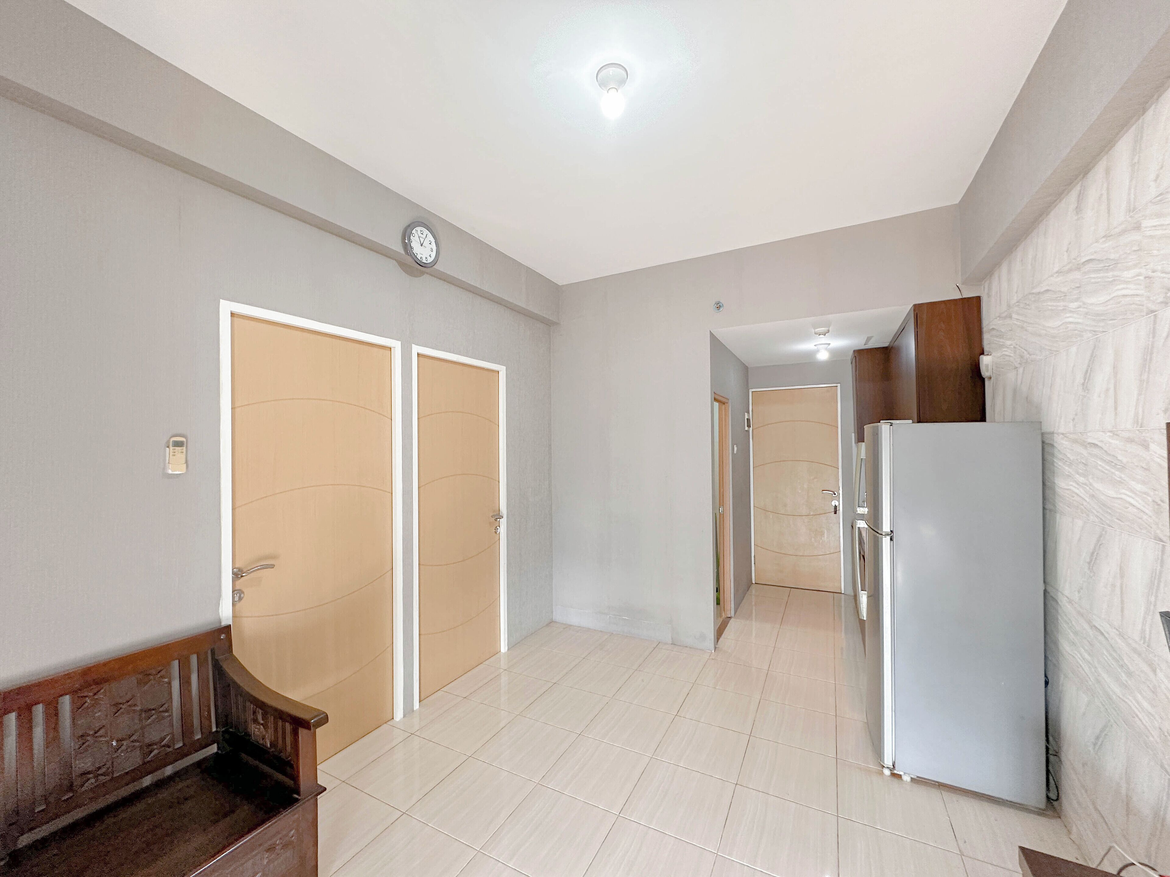 A spacious room with a tiled floor, a refrigerator, and a clock on the wall.