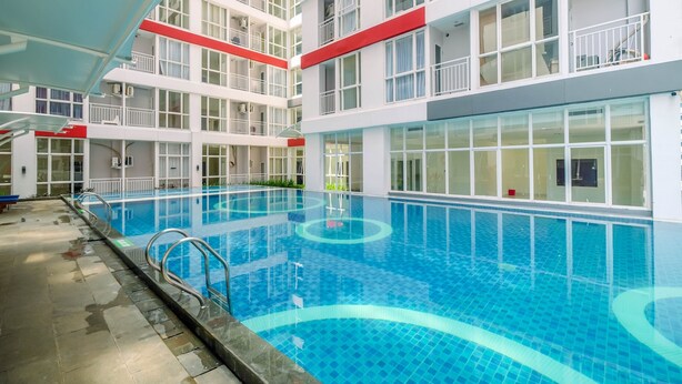 A modern indoor swimming pool with clear blue water, surrounded by a multi-story building with balconies and large windows. - Comfort Studio Taman Melati Margonda Apartment (Depok)