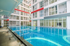 A modern indoor swimming pool with clear blue water, surrounded by a multi-story building with balconies and large windows. - Comfort Studio Taman Melati Margonda Apartment (Depok)