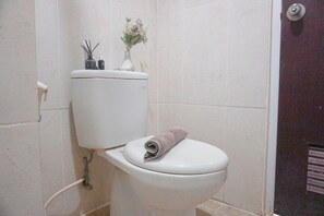 Eine Toilette mit einem aufgerollten Handtuch auf dem Sitz und einer Vase mit Blumen auf dem Tank.
