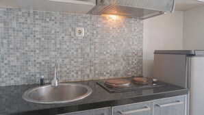 A kitchen with a stainless steel sink, a tiled backsplash, and a black countertop. - Comfort Studio Taman Melati Margonda Apartment (Depok)